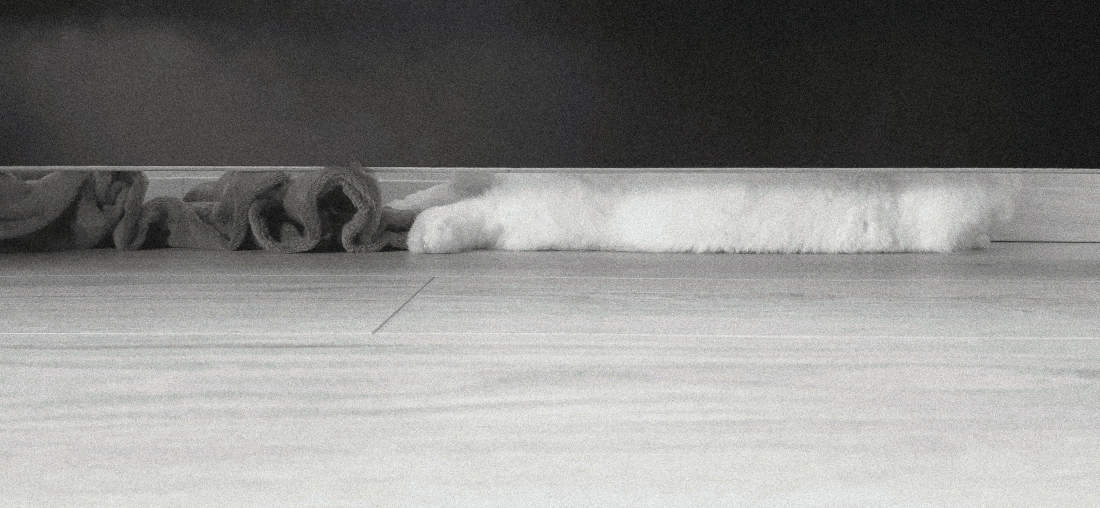 A black and white pocket printer style photo of a bunny lying on a bare wooden floor who pushed a blanket behind them.