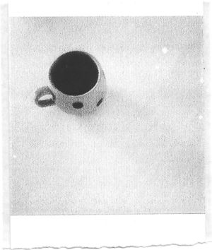 A black and white pocket printer style photo of a cofee cup on an otherwise empty table.