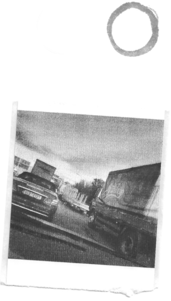 A black and white pocket printer style photo of cars in a traffic jam taken from inside a car. Above the photo, there is a simple circle painted in ink depicting the moon.